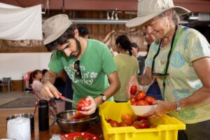 Man and woman, both wearing hats, cleaning tomatoes.