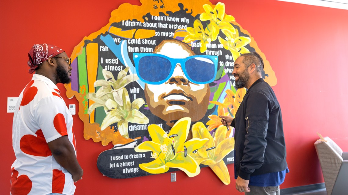 Monti Wilkins, left, director of Morrison Hall, and Jesse Wright, an artist and Ithaca High School teacher, talk after a section of tableaux dedicated to Toni Morrison was installed in Morrison Hall. Hanging near an image of Morrison, this painting on wood panels features Ithaca High senior London Smith, whose blue sunglasses reference Morrison’s novel, “The Bluest Eye.” Jason Koski/Cornell University