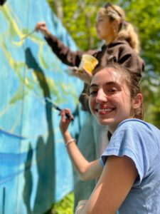 Person holding paintbrush in front of mural