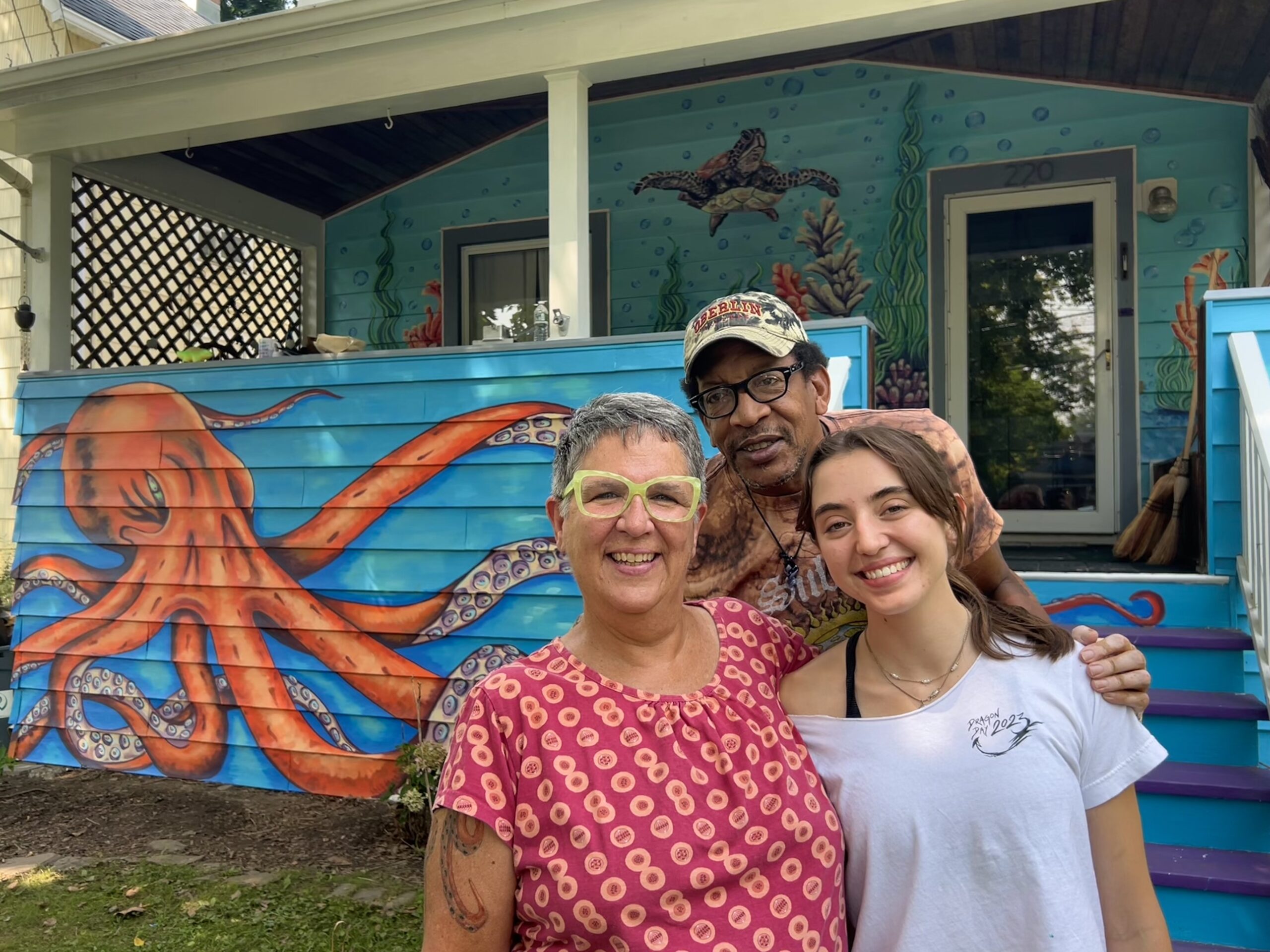 Pilar Garcia ’27 with Liddy Allee and Ricky Crawford in front of their house with mural in Ithaca's Fall Creek neighborhood. photo/provided