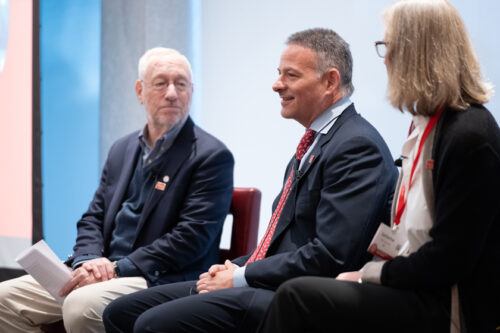 Three people, two men and one woman sit on stage during a panel discussion